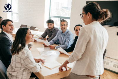 Confident female leader presenting ideas to an engaged diverse team around a sunlit conference table at Verbossa