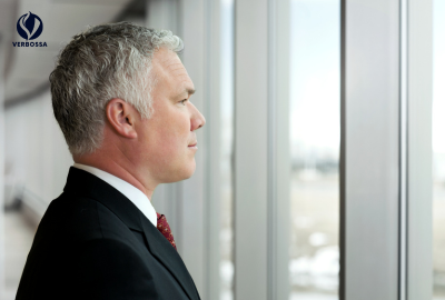 Distinguished silver haired leader in suit gazing thoughtfully out airplane window branded with Verbossa logo
